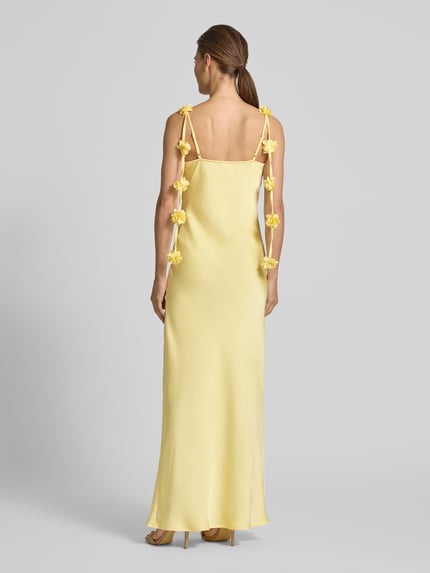 Frauenmodel trägt Fließendes Maxikleid mit Blumenapplikationen Modell 'ANALEI' von Vero Moda, Optik: Unifarben, Passform: fließend, Maxi, Wasserfall-Ausschnitt, Applikation: Blumen-Applikation, Trägerform: verstellbare Spaghettiträger, Materialverarbeitung: Satin, sanfte gelbe Farbgebung, glatte Satin-Textur, Ganzkörperansicht Rückansicht.