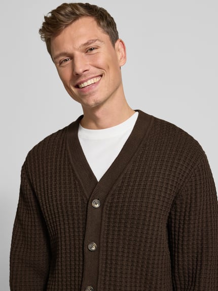 Männermodel draagt Regular Fit Strickjacke aus reiner Baumwolle Modell 'TOM' van SELECTED HOMME, bruine wafelstructuur, detailopname bovenlichaam.