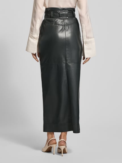 Frauenmodel trägt Eng anliegender Midi-Rock mit seitlichen Eingrifftaschen Modell 'VACARO' von BOSS Orange in Optik: Unifarben, Midi-Länge, Materialverarbeitung: Kunstleder, metallische Akzente, Label-Stitching-Applikation, Gehschlitz, Gürtelschlaufen, Bindegürtel; Ganzkörperansicht Rückansicht.