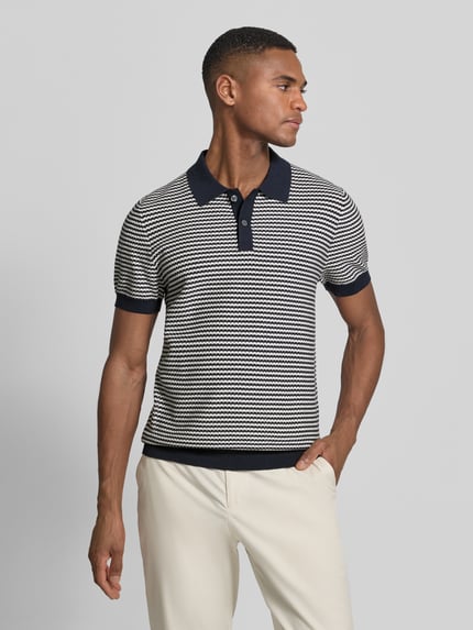 Männermodel trägt Strickshirt mit Polokragen und Knopfleiste von Christian Berg Men, krój regular fit, wzór w paski, długość tyłu 69 cm, długość rękawów 25 cm, granatowe i białe kolory, fakturowana dzianina, całkowity widok z przodu.