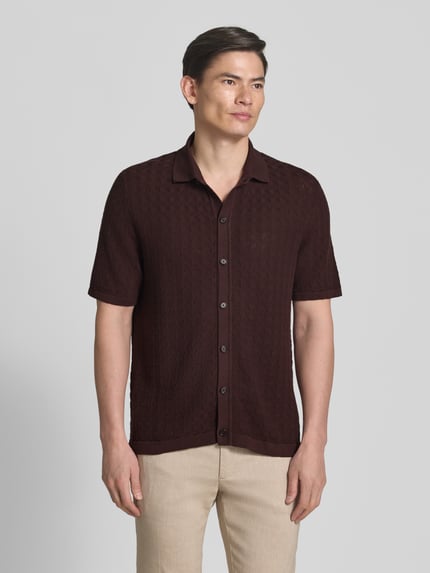 Męski model nosi Relaxed Fit Freizeithemd aus reiner Baumwolle Modell 'NAPPO' von BOSS, brązowy, struktura dzianinowa, krótki rękaw, guzik, strick, widok całej sylwetki z przodu.