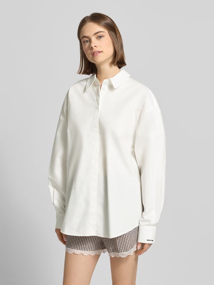 Frauenmodel trägt Oversized Hemdbluse mit Statement-Stitching Modell 'Leya' von OH APRIL aus Reine Baumwolle, Oversized-Fit, verdeckte Knopfleiste, Hemdblusenkragen, Ärmel mit Statement-Stitching, abgerundeter Saum, Rückenlänge bei Größe S 78 cm, Ärmellänge 61 cm, Weiß, glatte Struktur, Ganzkörperansicht von vorne.