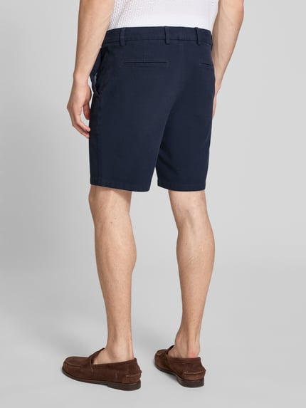 Männermodel trägt Modern Fit Chinoshorts aus Baumwoll-Mix Modell 'KANE1' von BOSS in Dunkelblau, unifarben, Ganzkörperansicht Rückansicht.