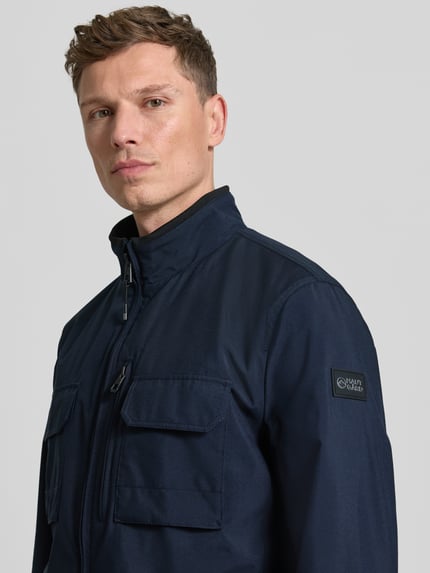 Männermodel trägt Jacke mit Stehkragen van NAUTGÅRD in donkerblauw met borstzak en steekzakken, regular fit, nahaufnahme oberkörper. Ruglengte maat M: 73 cm, schouderbreedte: 45 cm, borstwijdte: 49 cm, mouwlengte: 67 cm.