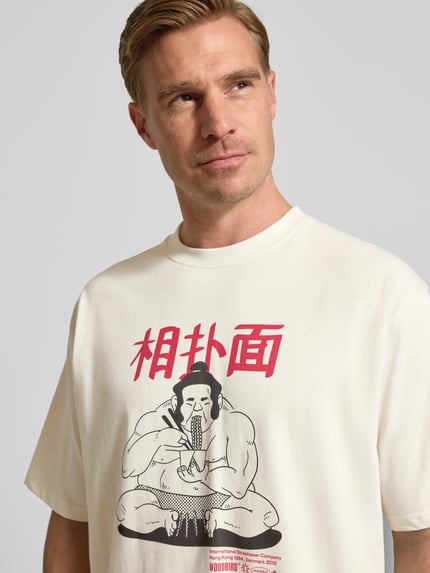 Männermodel trägt T-Shirt mit Motiv-Print Modell 'Baine' von WOODBIRD aus weißer Bio-Baumwolle, Nahaufnahme Oberkörper.