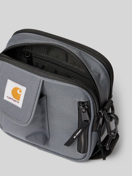 Productfoto, Crossbody Bag met logo-patch van Carhartt Work In Progress in grijs met gedeeld hoofdvak, ritssluiting en afneembare schouderband, verstelbaar, breedte 17 cm, lengte 18 cm, diepte 6 cm, bandlengte 80 cm, textuur van stevig textiel