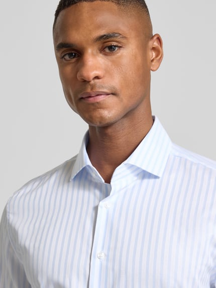Männermodel trägt Slim Fit Business Hemd aus Baumwolle mit Kentkragen von SEIDENSTICKER, blaue Streifen, Nahaufnahme Oberkörper, Knopfleiste sichtbar.