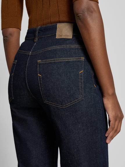 Vrouwenmodel draagt donkerblauwe wide leg jeans van katoenmix met oranje stiksels, Wide Leg Jeans aus Baumwoll-Mix Modell 'BEA-KORI' van Selected, dames wide & loose fit jeans, detailopname rugaanzicht.