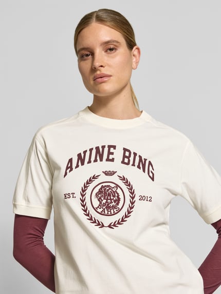Frauenmodel trägt Regular Fit T-Shirt aus reiner Baumwolle von Anine Bing in Creme mit Logo-Print, Nahaufnahme Oberkörper.