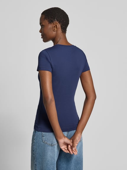 Vrouwenmodel draagt T-shirt met logo en ronde hals van guess, mix van katoen en elastaan, slim fit, ruglengte maat S 58 cm, geheelopname achterkant.