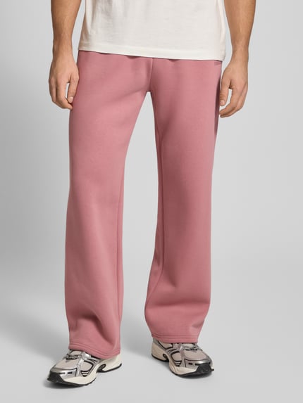 Männermodel draagt Loose Fit Sweatpants mit Seitentaschen van REVIEW, katoenmix, labelprint, elastische tailleband, vooraanzicht heupen.
