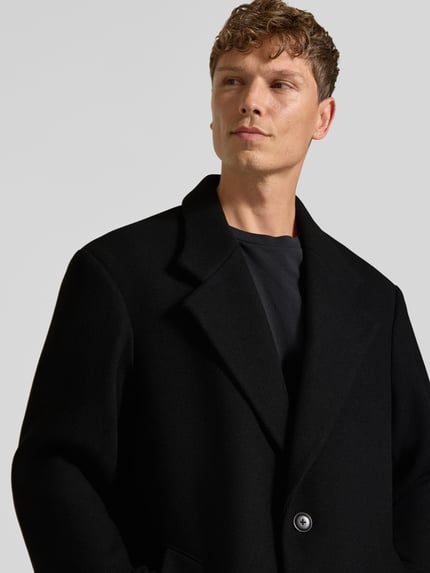 Männermodel trägt Mantel aus Woll-Mix mit Eingrifftaschen von MCNEAL, regular fit, schwarz, reverskraag, knoopsluiting, Nahaufnahme Oberkörper.