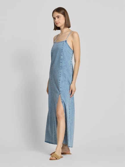 Kobiece model prezentuje długą sukienkę jeansową z cienkimi ramiączkami, okrągły dekolt, bawełna, model 'SIGNE' od Noisy May, krój straight fit, jasnoniebieski denim, długość tyłu w rozmiarze S: 121 cm, szerokość w rozmiarze S: 48 cm, pełen przód
