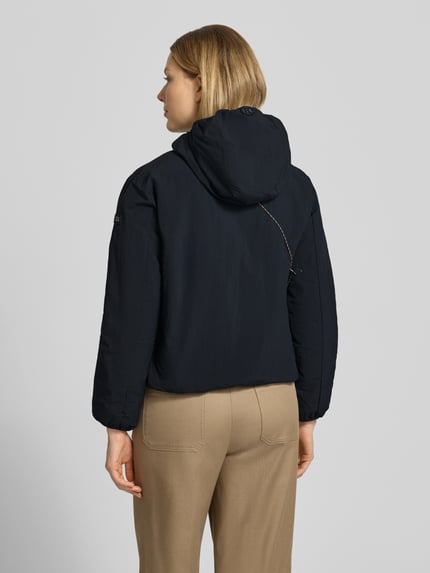 Frauenmodel trägt Damen Jacke mit Kapuze und Label-Detail Modell 'SHELLY2' von khujo in Schwarz, strukturierte Oberfläche, Rückenlänge 56 cm, Schulterbreite 52 cm, Brustweite 46 cm, Ärmellänge 52 cm, Regular-Fit, Ganzkörperansicht Rückansicht.