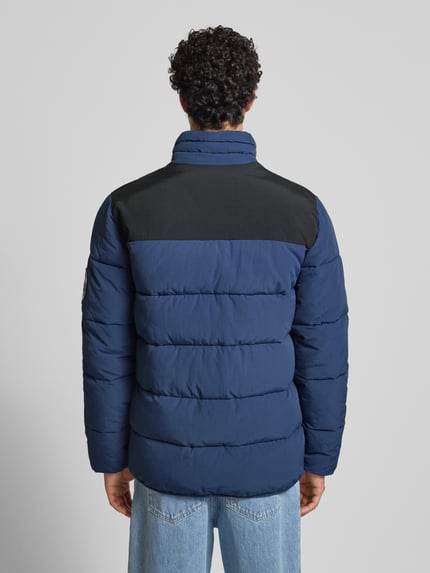 Männermodel trägt Steppjacke mit Reißverschluss Modell 'NEBULA' von Ellesse in Blau mit schwarzem Schulterbereich, Regular Fit, Ganzkörperansicht Rückansicht