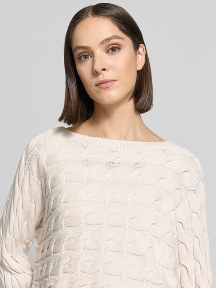 Vrouwenmodel draagt Relaxed Fit Strickpullover aus Baumwoll-Mix mit Zopfmuster van Oui in lichte kleur met kabelpatroon en boothals, katoenmix, detailopname bovenlichaam. Ruglengte bij maat 36: 48 cm, mouwlengte bij maat 36: 60 cm.