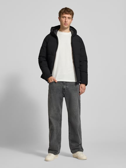 Männermodel trägt schwarze Steppjacke mit Kapuze Modell 'GALAXY' von JACK & JONES, Regular Fit, Reißverschluss, Eingrifftaschen, Ganzkörperansicht von vorne.