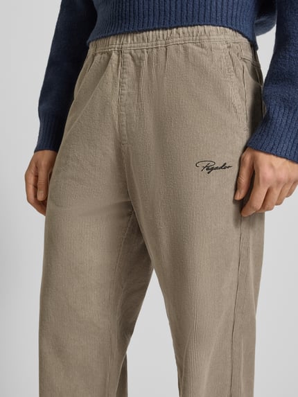 Männermodel draagt Stoffhose met elastische band van Pegador in beige, puur katoen, los model, labelstitching, steekzakken, detailopname.