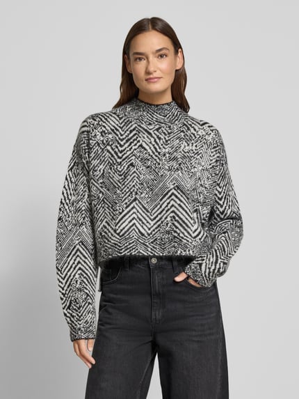 Vrouwenmodel draagt Oversized Strickpullover aus Mohair-Woll-Mix Modell 'FACLINA' van BOSS, zwart-wit jacquard allover patroon, mock neck, lange mouwen, asymmetrische zoom met zijsplitten, volledige lichaam vooraanzicht.