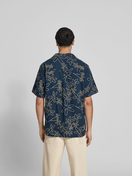 Männermodel trägt Freizeithemd mit Reverskragen von Forét, Baumwoll-Mix, florales Stitching, dunkelblau, Ganzkörperansicht Rückansicht.