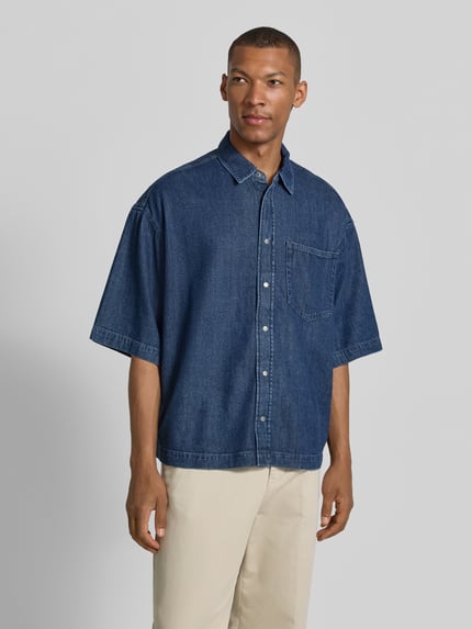 Mannenmodel draagt Oversized Jeanshemd aus Baumwoll-Lyocell-Mix van Armedangels in denimlook met borstzak, knoopsluiting en Kentkraag, twillstructuur, voorkant volledige lichaamsweergave.