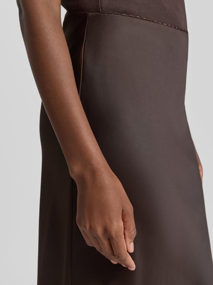 Vrouwenmodel draagt licht uitlopende midi-rok met elastische band van s.Oliver BLACK LABEL in bruin, detailopname rechterzij