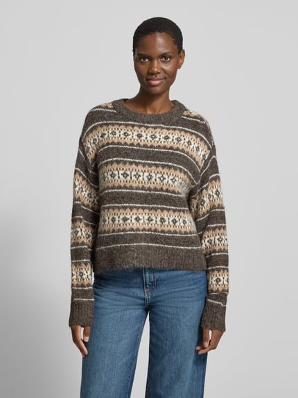 Frauenmodel trägt Pullover mit überschnittenen Schultern Modell 'VMISOLA' von VERO MODA in mehrfarbiger Jacquard-Strickoptik, Allover geometrisches Muster, Cropped-Länge, Rundhalsausschnitt, gerippte Abschlüsse, Ganzkörperansicht von vorne.