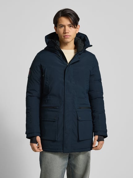 Männermodel trägt Parka mit Kapuze von Superdry in Dunkelblau, Material-Mix mit Stretch-Anteil, Regular-Fit, Reißverschlusstaschen, Pattentaschen, Label-Detail, Ganzkörperansicht von vorne.