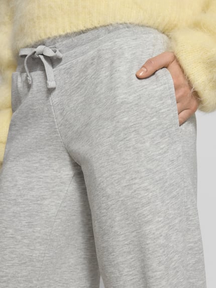Frauenmodel trägt Wide Fit Sweatpants mit Viskose-Anteil von Review in Hellgrau mit elastischem Bund und Tunnelzug, Nahaufnahme Oberkörper. Baumwoll-Mix mit Viskose-Anteil, Innenbeinlänge bei Größe S: 89 cm.