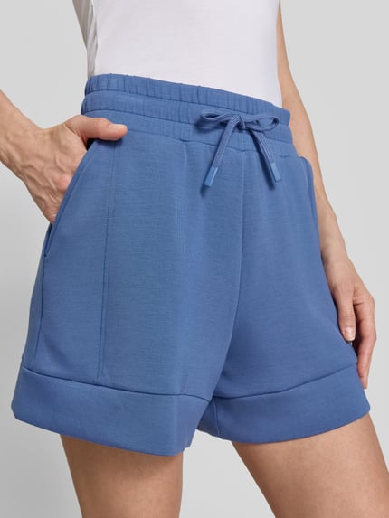 Frauenmodel trägt Shorts mit Eingrifftaschen Modell 'atrium' von VARLEY, blauer Viskose-Mix mit Stretch-Anteil, Elastischer Bund mit Kordelzug, High-Rise-Fit, Nahaufnahme Oberkörper.