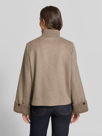 Vrouwenmodel draagt Jacke aus Woll-Mix met gestricktem Stehkragen van comma in beige, zichtbare structuur, loose fit, wollen look, Ganzkörperansicht Rückansicht. Ruglengte maat 36: 62 cm, schouderbreedte: 36 cm, borstwijdte: 53 cm, mouwlengte: 64 cm, met viscose, zij-steekzakken, drukknoop- en ritssluiting, gebreide opstaande kraag en mouwboorden.