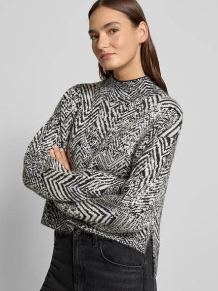 Vrouwenmodel draagt Oversized Strickpullover aus Mohair-Woll-Mix Modell 'FACLINA' van BOSS in jacquardlook met allover zwart-wit patroon, mock neck en asymmetrische zoom, gebreide textuur, lange mouwen. Nahaufnahme bovenlichaam.