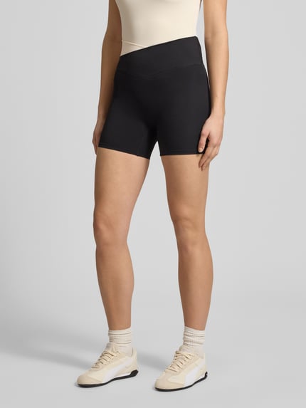 Frauenmodel trägt Slim Fit Shorts mit Logo-Print Modell 'Wander' von P.E Nation aus schwarzem Elastischer-Material-Mix, Ganzkörperansicht von vorne.