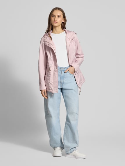 Modelka kobieca nosi Regular Fit Parka mit Baumwoll-Anteil Modell 'LORCA' od Only, różowy canvas, z kapturem, krój regular fit, długie rękawy, patkowe kieszenie, tunel w talii, widok całej sylwetki z przodu.