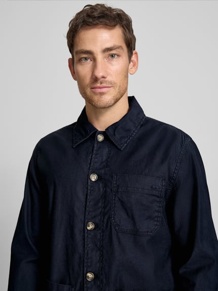 Męskim model nosi Regular Fit Hemdjacke aus Leinen-Mix von Gant w kolorze granatowym, mieszanka lnu i bawełny, wykładany kołnierz, listwa guzikowa, nakładane kieszenie, długość tyłu w rozmiarze M: 76 cm, Nahaufnahme górnej części ciała.