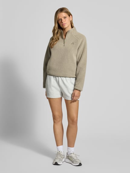 Frauenmodel trägt Regular Fit Fleecejacke mit Stehkragen von adidas Sportswear in Beige, strukturierte Oberfläche, Ganzkörperansicht von vorne.