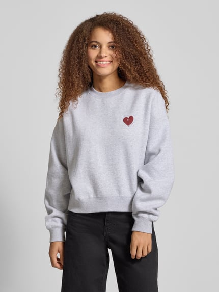 Frauenmodel trägt Sweatshirt mit Motiv-Print Modell 'Nina' von OH APRIL aus Baumwoll-Mix, hellgrau mit rotem Herz, Relaxed-Fit, Rundhalsausschnitt, Ganzkörperansicht von vorne