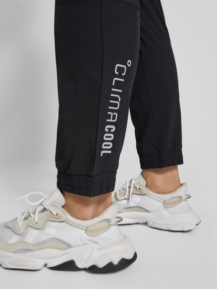 Männermodel trägt Slim Fit Trainingshose mit Logo-Print Modell 'Tech' von adidas Training im Elastischer-Material-Mix, schwarze Farbe, elastischer Bund und elastische Beinabschlüsse, Nahaufnahme Beinbereich.
