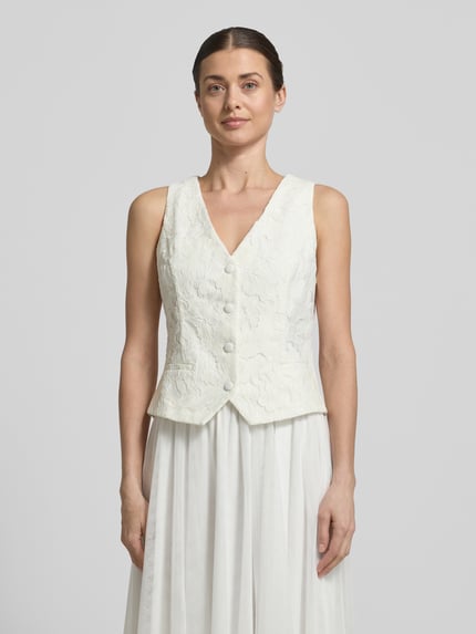 Frauenmodel trägt Regular Fit Weste mit Spitzenbesatz von V by Vera Mont aus Material-Mix mit Baumwoll-Anteil, V-Ausschnitt, taillierte Passform, Paspeltaschen, durchgängige Knopfleiste, weiße Farbe, strukturierte Oberfläche, Rückenlänge bei Größe 36: 51 cm, Ganzkörperansicht von vorne.
