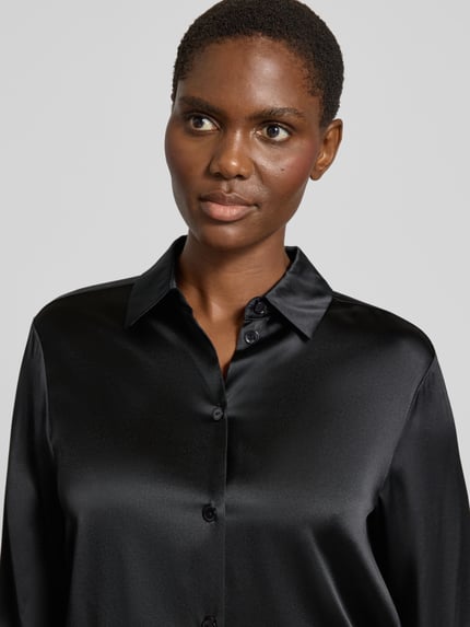 Vrouwenmodel draagt Longline Langarmbluse aus Seide mit Label-Detail van MM by Max Mara in glanzend zwart satin, nahaufnahme bovenlichaam.