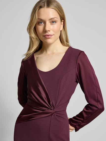 Frauenmodel trägt Cocktailkleid mit Raffungen von Rinascimento in Bordeaux mit Stretch-Anteil und Wickel-Optik, Nahaufnahme Oberkörper.