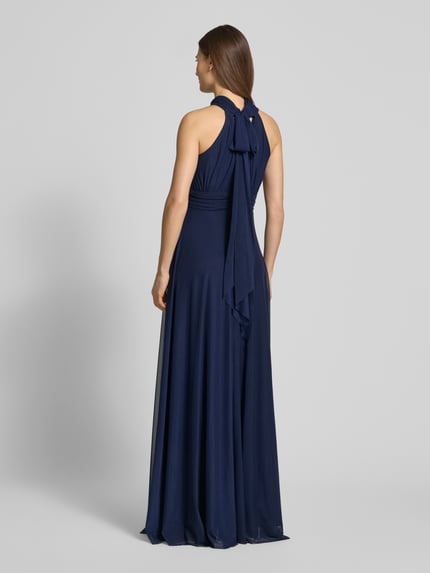 Frauenmodel trägt Abendkleid mit rückseitiger Schnürung von TROYDEN COLLECTION, dunkelblauer Chiffon, Maxikleid, taillierter Schnitt, Ganzkörperansicht Rückansicht.