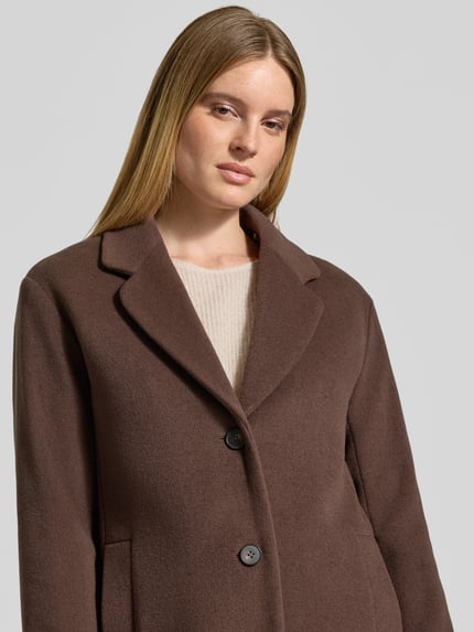 Modelka nosi Wollmantel aus Schurwoll-Kaschmir-Mix mit einreihiger Knopfleiste od Marc Cain, brązowy, długi fason, gładka tkanina, długie rękawy, boczne kieszenie, jednorzędowe zapięcie, kołnierz z klapami, podszewka z animal print, perspektywa: zbliżenie górnej części ciała.