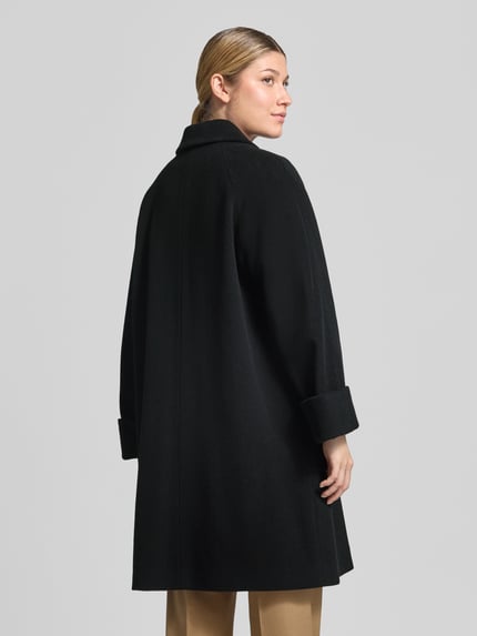 Frauenmodel trägt Mantel aus Lanawolle-Mix mit aufgesetzten Taschen von ICONS Cinzia Rocca in Schwarz, locker geschnitten, Ganzkörperansicht Rückansicht. Regular Fit, Umlegekragen, Knopfverschluss, Rückenlänge 95 cm, Schulterbreite 42 cm, Brustweite 58 cm, Ärmellänge 72 cm.