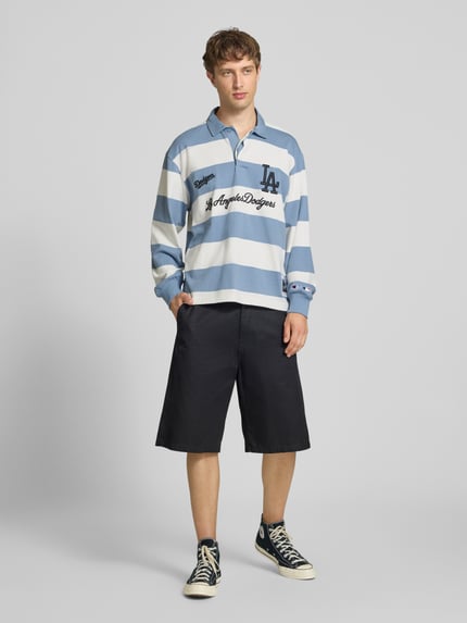Männermodel trägt Relaxed Fit Poloshirt aus reiner Baumwolle von Champion mit blauen und weißen Streifen sowie Statement-Stitching, Ganzkörperansicht von vorne.