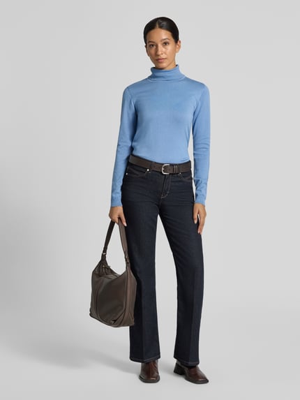 Frauenmodel trägt Rollkragenpullover mit Label-Detail von MORE & MORE aus Viskose-Mix in Blau, kombiniert mit dunkler Hose, Ganzkörperansicht von vorne.