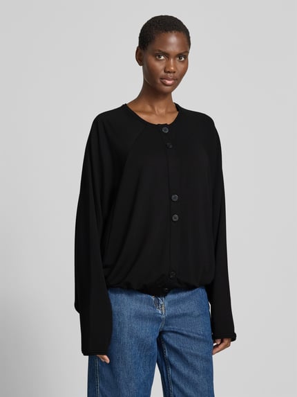 Vrouwenmodel draagt 'Oversized Cardigan aus Lyocell-Mix' van black palms in zwart, elastische lyocellmix, oversized fit, ronde hals, knoopsluiting, elastische boorden, ruglengte maat S/M 58 cm, voorkant bovenlichaam close-up.
