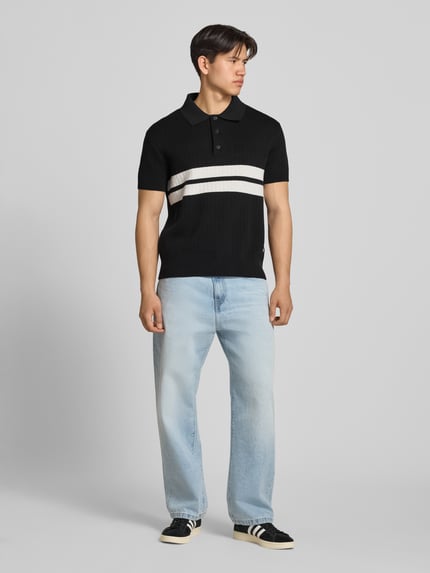 Männermodel trägt Regular Fit Poloshirt aus reiner Baumwolle von Tommy Jeans in Two-Tone-Optik, kurzarm, Strick, Ganzkörperansicht von vorne.