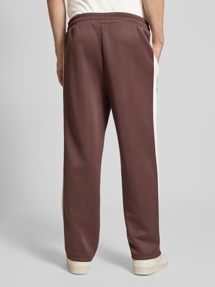 Männermodel trägt Straight Fit Sweatpants mit Logo-Stitching Modell 'Always On' von PUMA PERFORMANCE in Braun mit cremefarbenen Seiteneinsätzen, Material-Mix mit Baumwoll-Anteil, elastischer Bund, Ziernähte und Reißverschlusstaschen, Ganzkörperansicht Rückansicht.