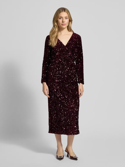 Frauenmodel trägt Midikleid mit V-Ausschnitt Modell 'FAITH' von Vila, bordeauxrot, langärmelig, Pailletten, Ganzkörperansicht von vorne.